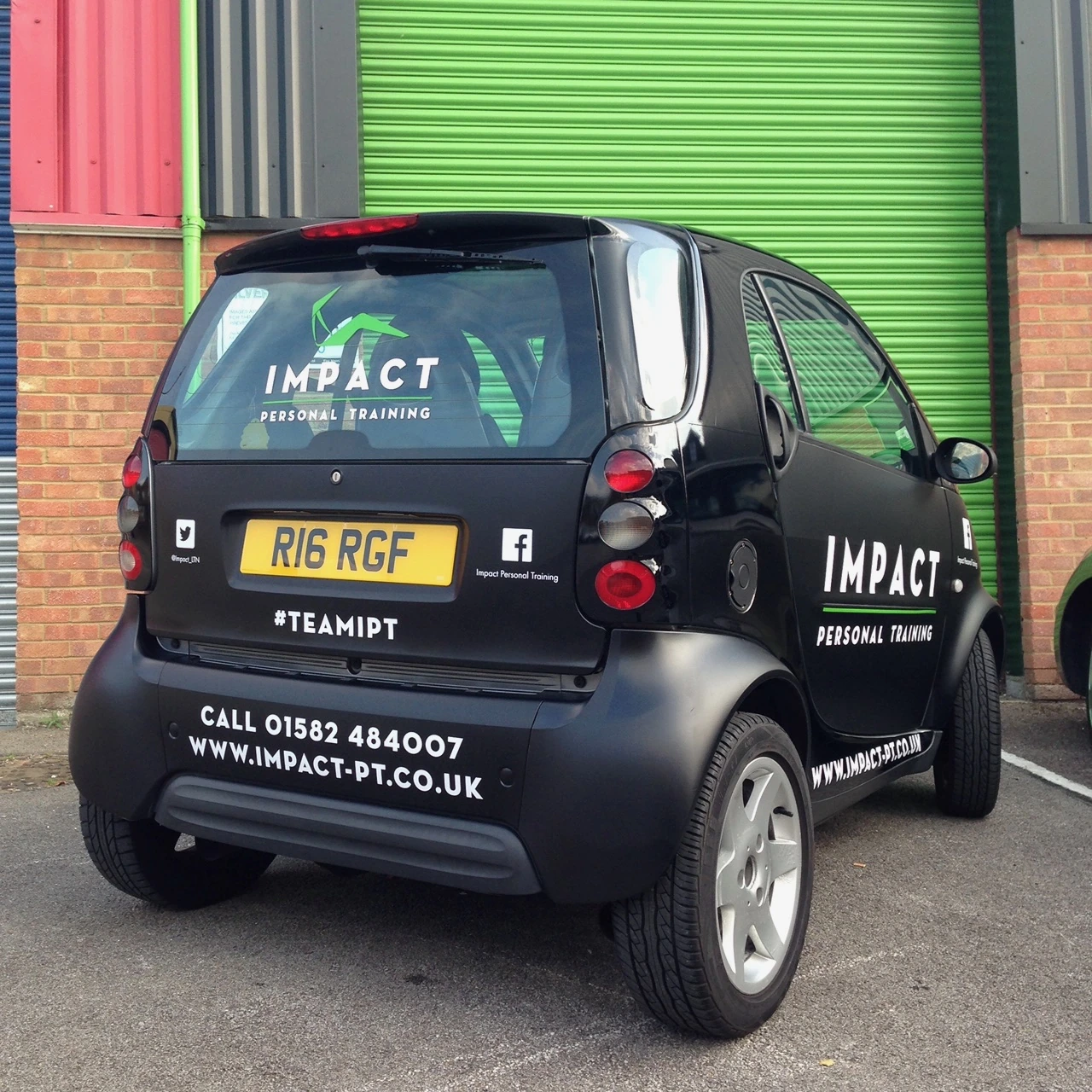 Rear view of the Impact Smart car, showing rear-window branding, contact details and social accounts